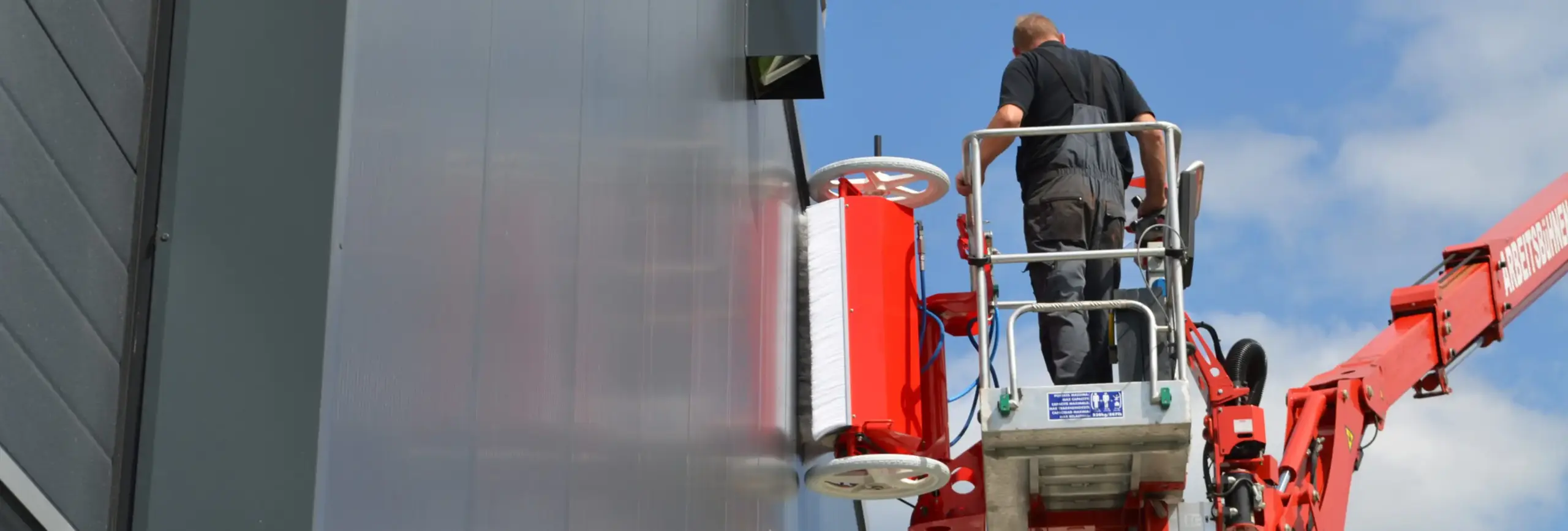 El robot de limpieza facadeBRUSH h-line limpia la fachada de un edificio controlado por un empleado